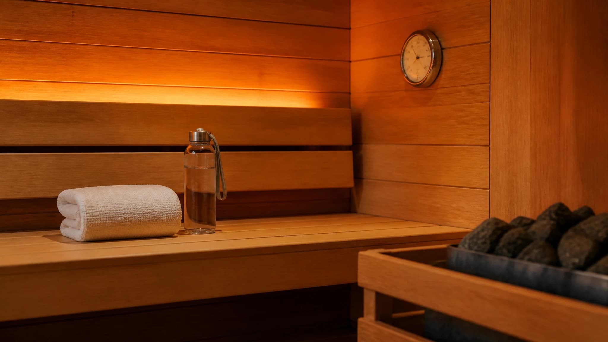 Wood-lined sauna with a thermometer, towel, and water bottle